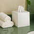 White | tissue box with tissues on a green surface next to folded towels, with Earthware logo.